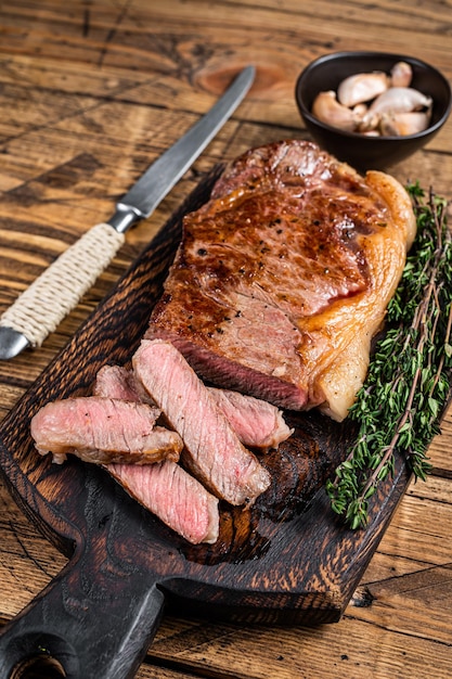 Bistecca o controfiletto di manzo alla griglia di new york a fette su una tavola di legno. fondo in legno. vista dall'alto.