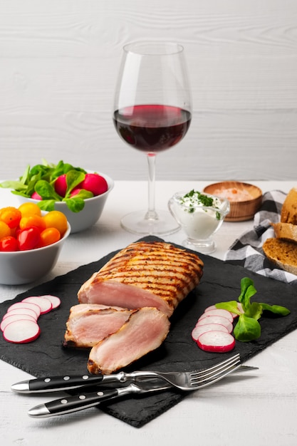 Sliced grilled pork fillet with fresh tomatoes and raddish served with glass of red wine.