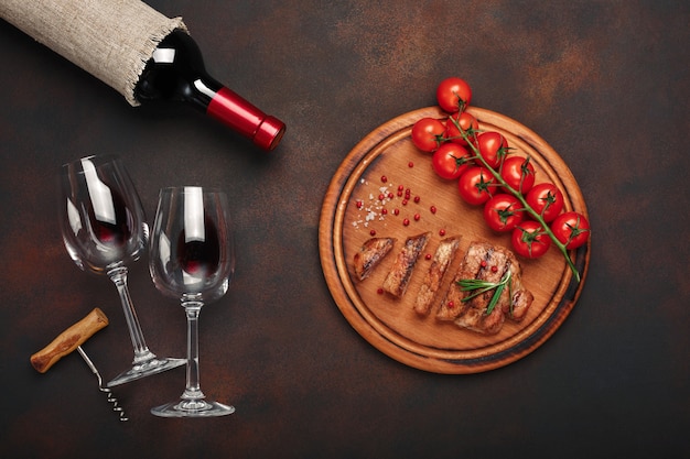 Sliced grilled pork steaks with bottle of wine, wine glass, corkscrew, cherry tomatoes and rosemary 