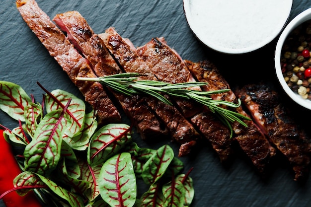 Sliced grilled steak medium rare served on black cutting board with vegetables