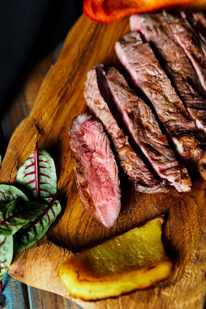 Sliced grilled steak medium rare served on wooden cutting board with vegetables