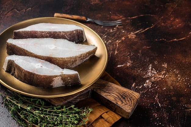 Sliced halibut fish, raw steaks on plate with thyme. Dark background. Top view. Copy space.