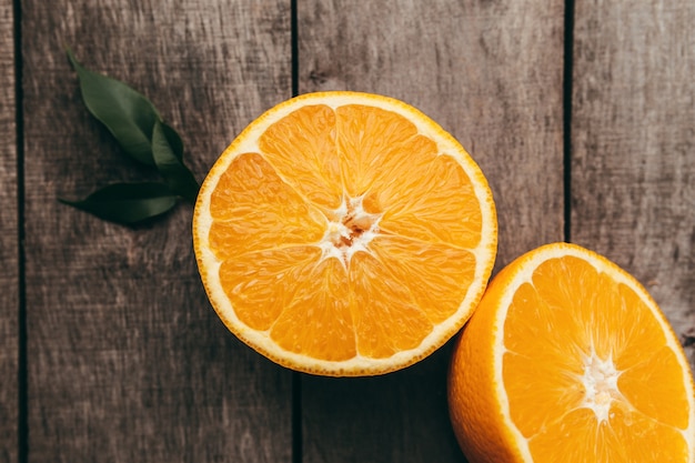 Sliced halves of orange fruit on gray wooden table pulp and green leaves