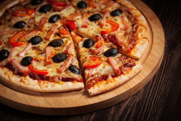 Sliced ham pizza with capsicum and olives on wooden board on table