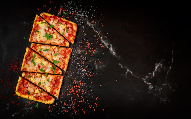 Photo sliced hawaiian pizza on black stone, top view.