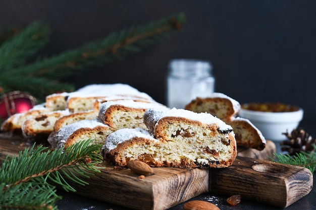 Sliced homemade Christmas dessert stollen with raisins and nuts on  rustic table with cinnamon. Christmas tree branches, selective focus