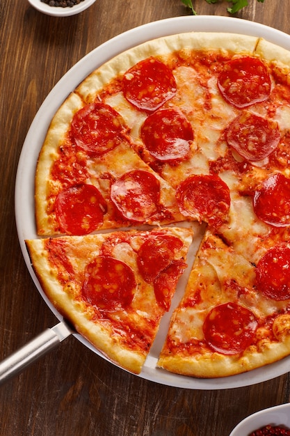 Sliced homemade pepperoni pizza on old rustic wooden table. Top view