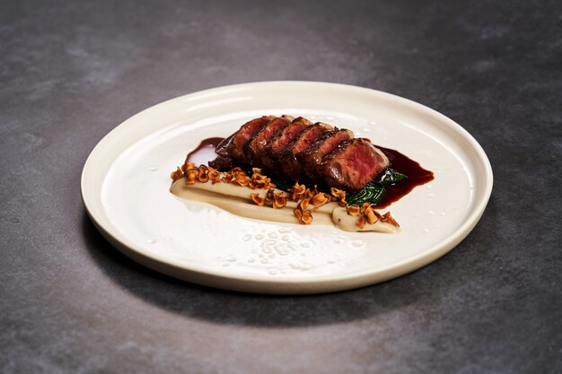 Sliced lamb meat and mashed potatoes on a white plate on gray table