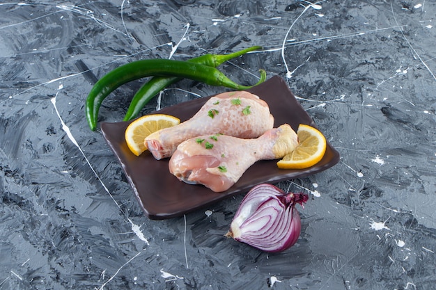 Sliced lemons and drumsticks on a platter next to vegetables , on the marble surface.