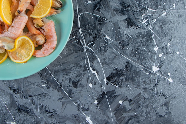 Sliced lemons and prawns on a plate, on the marble background. 