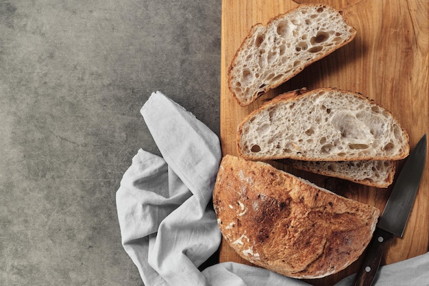 Sliced loaf of artisan sourdough bread on a cutting board on a gray concrete table Top view with copy space