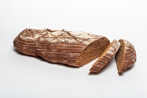 Sliced loaf of black rye bread with cuts from a knife on top of it and sprinkled with white flour isolated on a white background Healthy eating concept