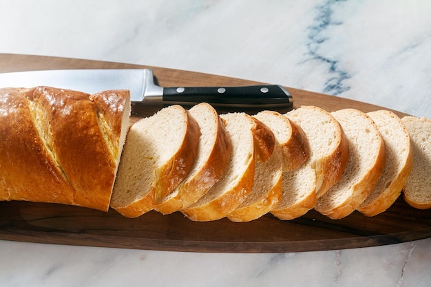 Sliced loaf of bread on a cutting board and a chef's knife on a marble table