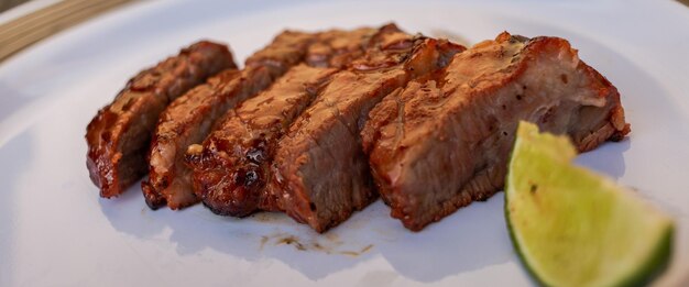 Sliced meat and a green wedge of lime on a plate