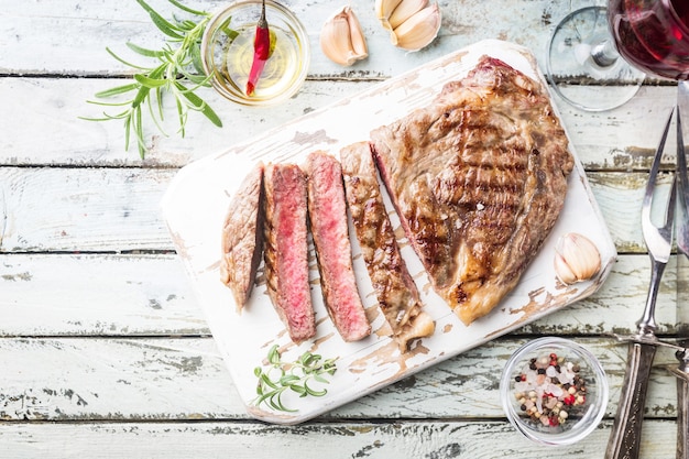 Sliced medium rare grilled beef steak on rustic cutting board with rosemary and spices