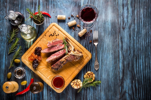 Sliced medium rare grilled t-bone steak on rustic wooden background with rosemary and spices