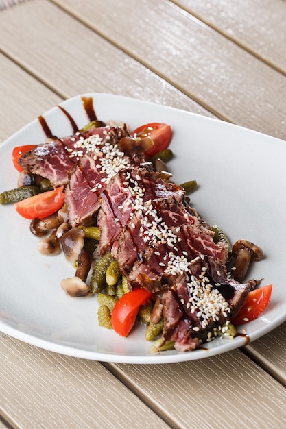 Sliced medium rare Roast beef with pickles, cherry tomatoes,mushrooms on a white plate