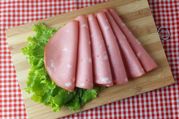 Sliced mortadella on cutting board in kitchen with checkered tablecloth