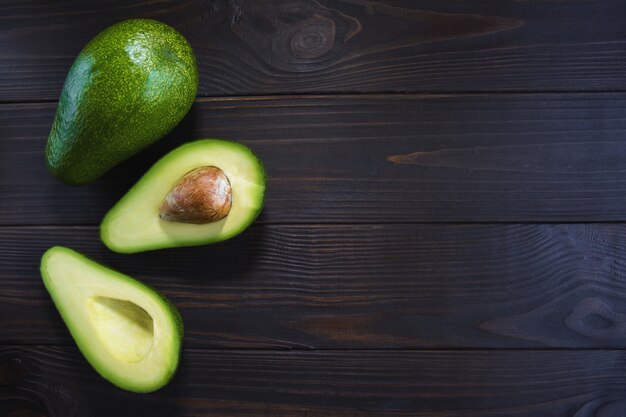 sliced ​​and one whole ripe and beautiful avocado on a dark wooden background with free space on the right