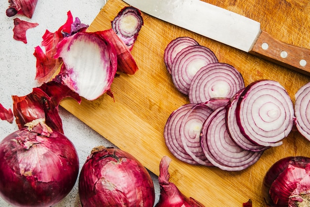 Photo sliced onion; knife and peels over wooden chopping board