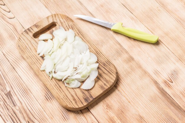 Sliced onions with half rings on a wooden chopping board on a wooden background