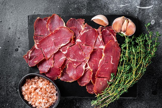 Sliced Pastrami roasted beef meat with herbs. Black background. Top view.