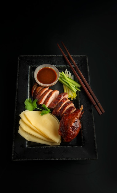 Sliced peking duck with pancakes on a plate on a black background