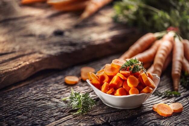 Sliced pieces of carrot in a bowl and a fresh bunch of carrots in the background.