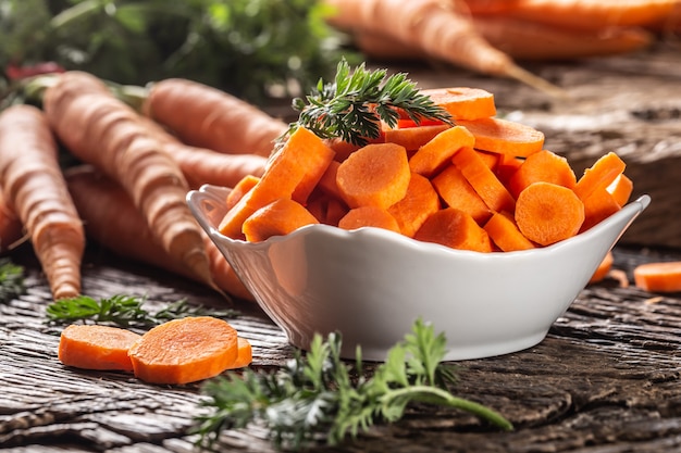 Sliced pieces of carrot in a bowl and a fresh bunch of carrots in the background.