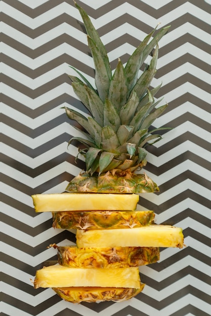 Sliced pineapple on graphic summer background. tropical fruit\
sliced pineapple rings. creative flat lay composition on black and\
white stripes pattern. top view