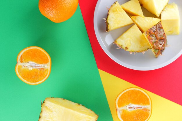 Sliced pineapple and oranges on multicolored background Pineapple and orange halves on white plate Close up