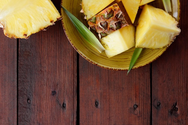 Sliced pineapple on yellow plate on wooden boards Pineapple with green leaves on wooden background Vegetarian food Copy space