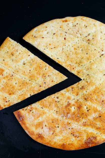 Sliced pizza on a black stone background, top view. Freshly baked focaccia with cheese