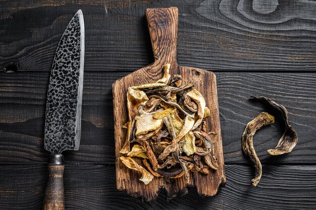 Foto porcini selvatici a fette di funghi secchi su un tagliere di legno. fondo in legno nero. vista dall'alto.