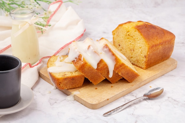 Sliced pound cake topped with lemon glaze on a cutting board and spoon are marble table.