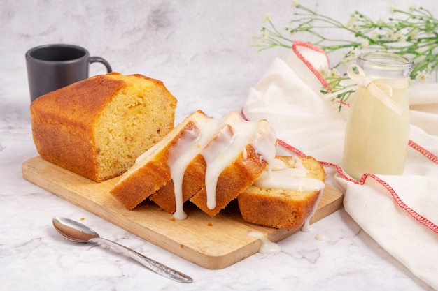 Sliced pound cake topped with lemon glaze on a cutting board and spoon are marble table.