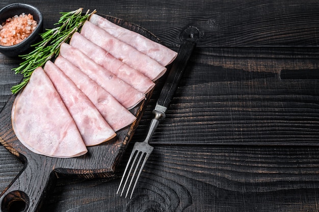 Sliced prosciutto ham on wooden cutting board on wooden table.\
top view.