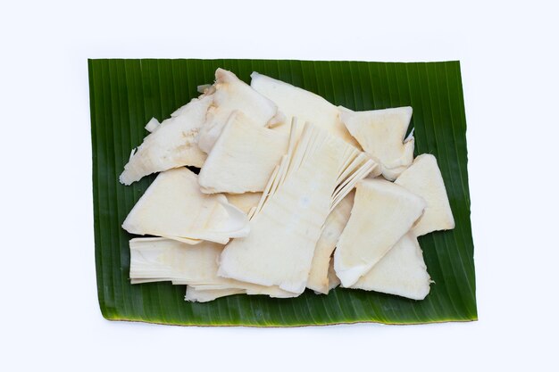 Sliced raw bamboo shoots on banana leaf on white background.