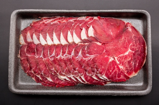 Sliced raw beef place in a row on a black plastic tray isolated on a black background. sliced ââmeat for cooking, fresh meat for grilling, yakiniku, sukiyaki or shabu.