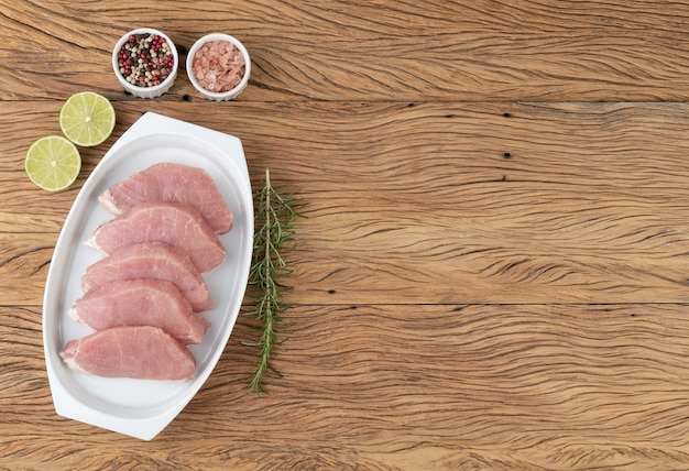 Sliced raw pork loin meat over white plate with seasonings and copy space.