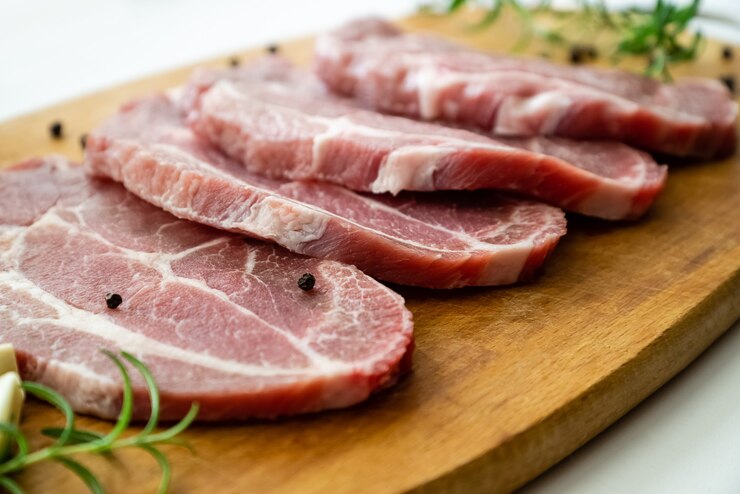 Photo sliced raw pork meat with fresh rosemary and pepper on cutting board