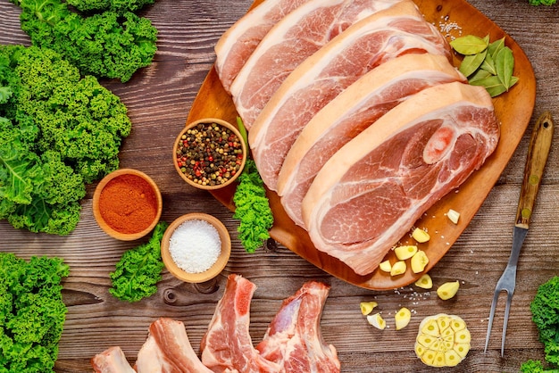 Sliced raw pork shoulder with spices and fork on wooden board