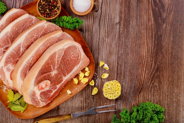 Sliced raw pork shoulder with spices and fork on wooden board