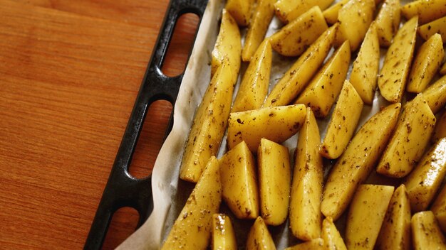 Photo sliced raw potatoes on a baking sheet with spices and rosemary, top view, copy space