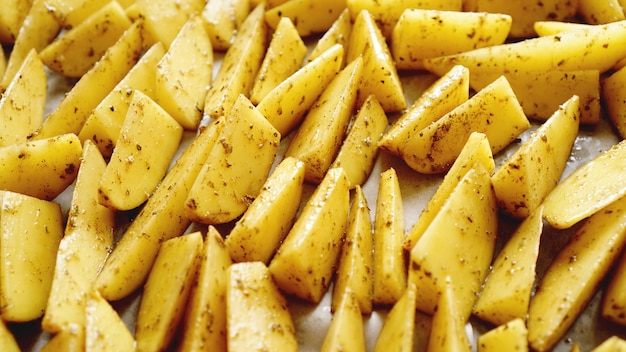 Sliced raw potatoes on a baking sheet with spices and rosemary, top view