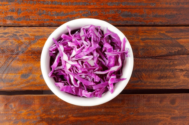 Sliced raw red cabbage in ceramic bowl over rustic wooden table Top View