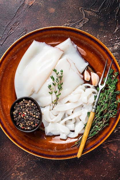 로즈마리와 함께 소박한 접시에 원시 링 오징어를 썰어. 어두운 배경입니다. 평면도.