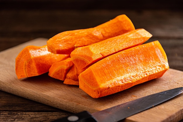 Sliced raw sweet carrots on a wooden cutting board with a knife.