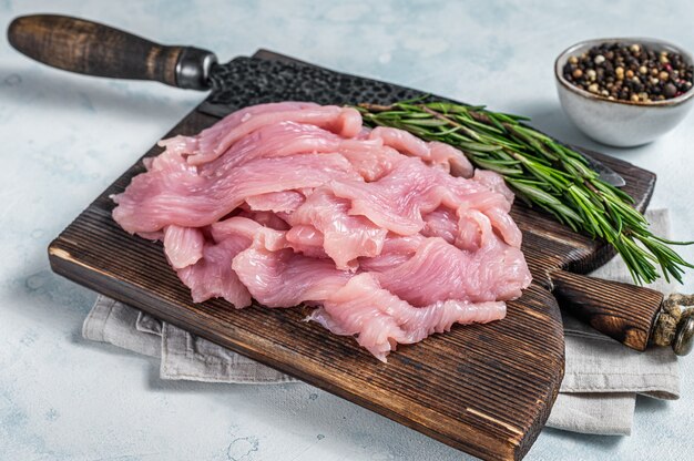 Tacchino crudo affettato o filetto di pollo su un tagliere con coltello da macellaio. vista dall'alto.