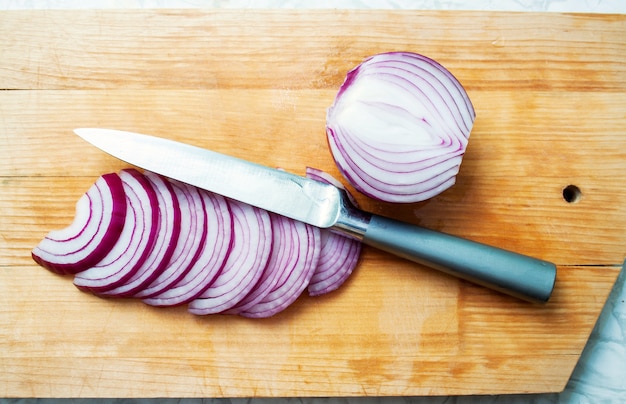 Sliced red onion and knife on a cutting wooden board